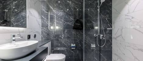 A modern bathroom with a large white sink, a toilet, and a glass-enclosed shower area.