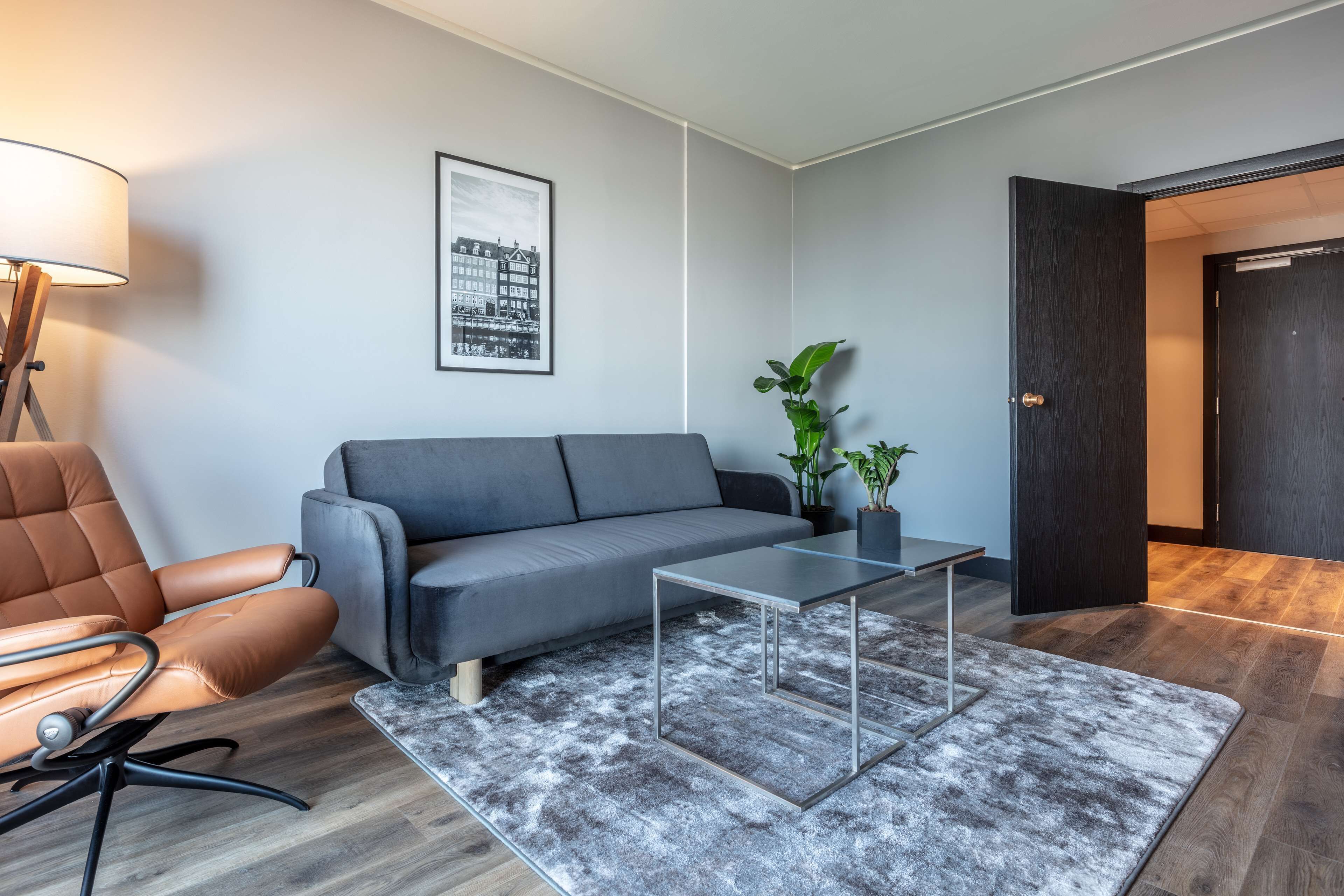 A modern living room with a grey sofa, a brown leather chair, a glass coffee table, and a grey shag rug.