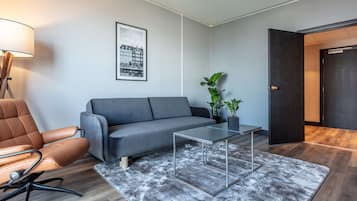 A modern living room with a grey sofa, a brown leather chair, a glass coffee table, and a grey shag rug.