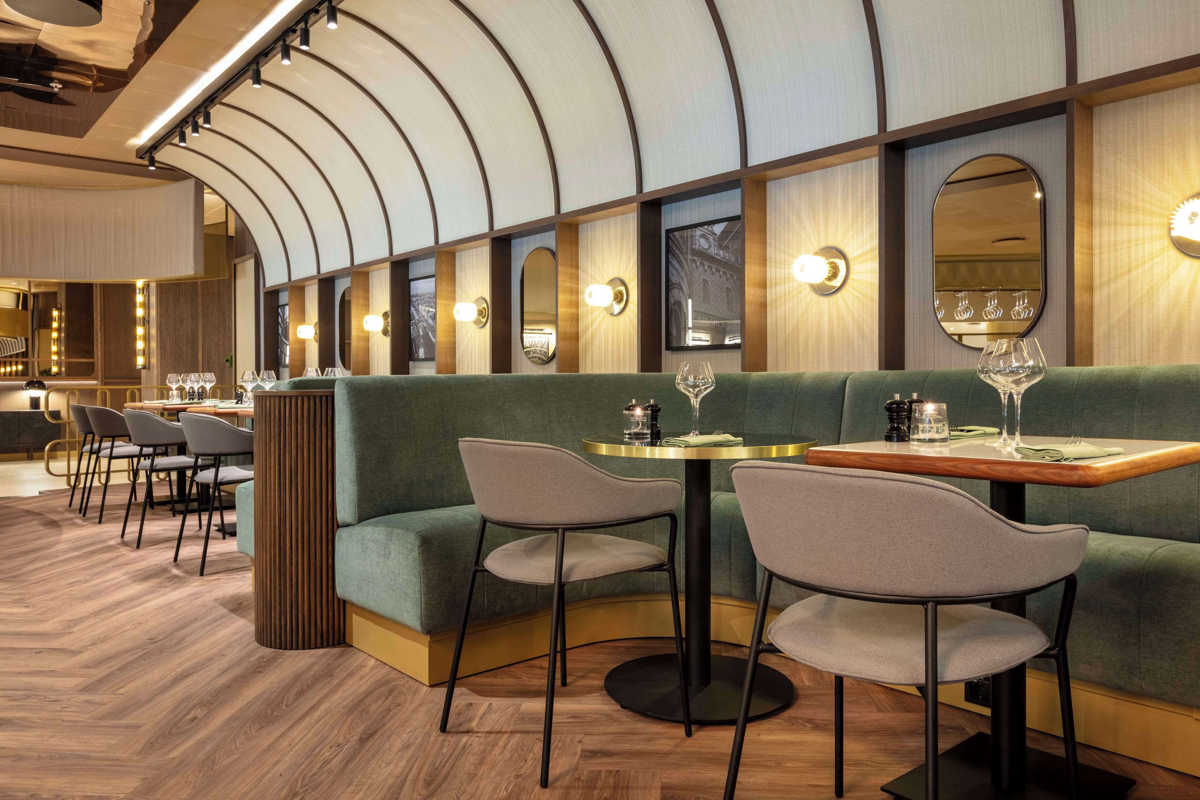 A restaurant with a green booth seating area, round tables, and a wooden floor.