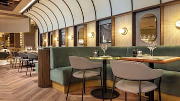 Um restaurante com área de estar em cabines verdes, mesas redondas e piso de madeira.