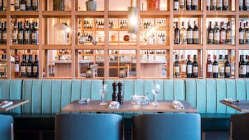 Un restaurante con estanterías de madera llenas de botellas de vino, una cabina acolchada de color verde y una mesa con copas de vino y cubiertos.