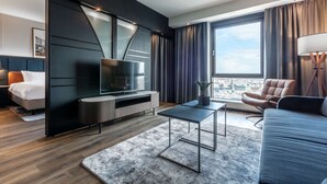 Une chambre d’hôtel moderne dotée d’une grande fenêtre, d’un téléviseur à écran plat, d’un canapé, d’une table basse et d’un lit avec une tête de lit.