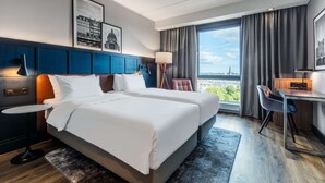 Une chambre d’hôtel avec deux lits, un bureau, une chaise, une lampe et une vue sur la ville.
