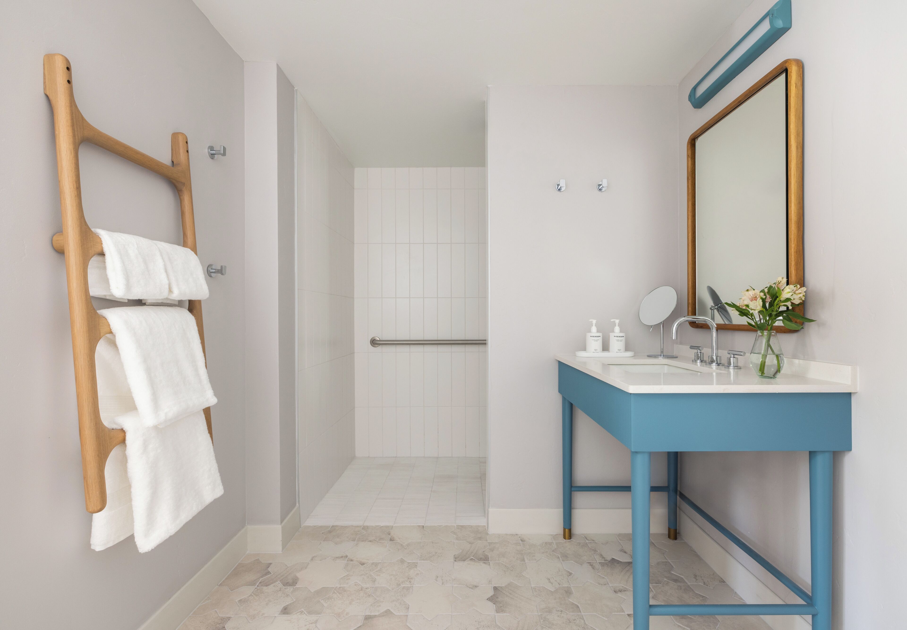 A bathroom with a shower, a towel rack, a sink with a mirror, and a vase with flowers.