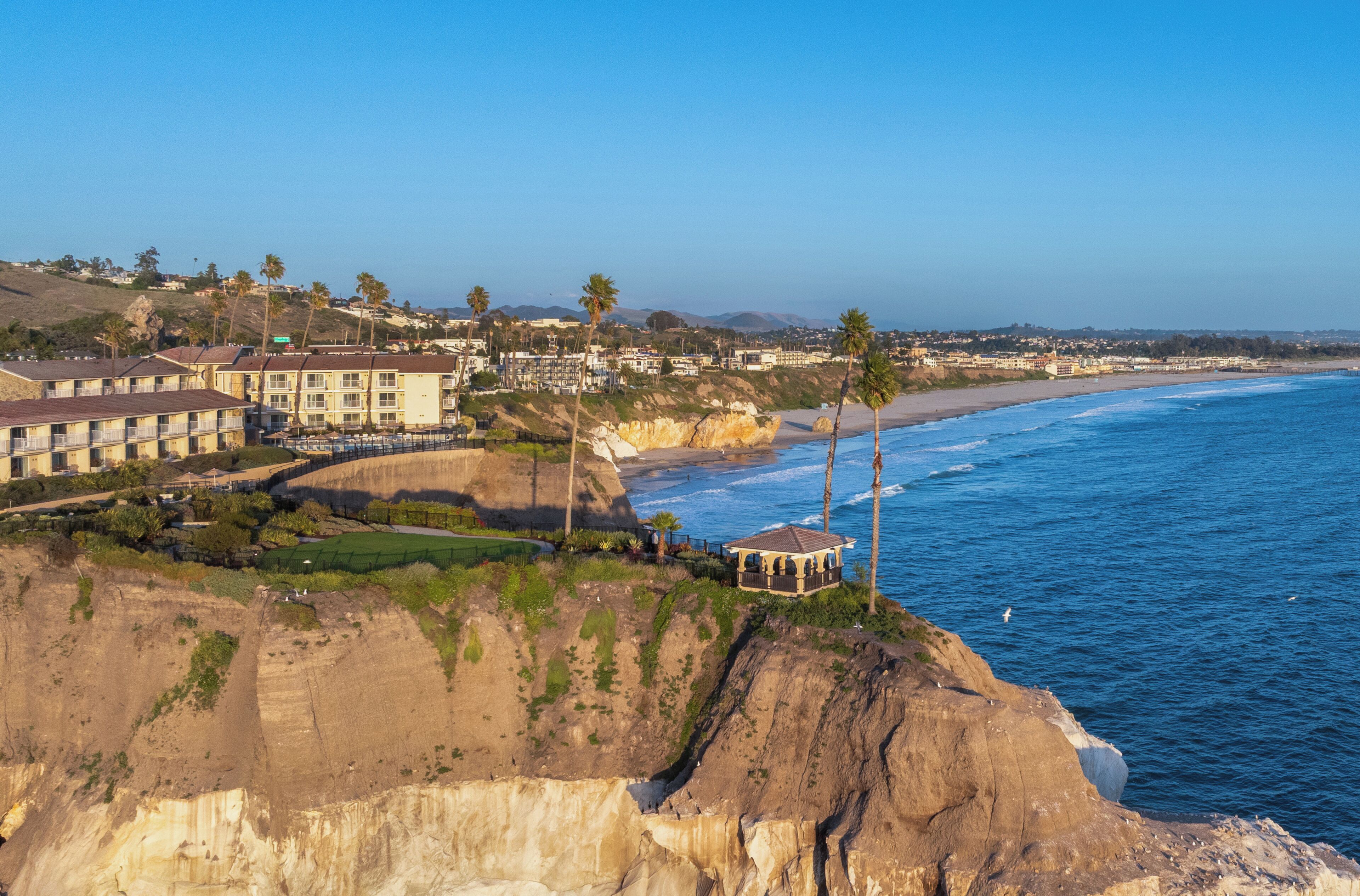 A coastal hotel with multiple buildings, a beach, and a cliff overlooking the ocean.