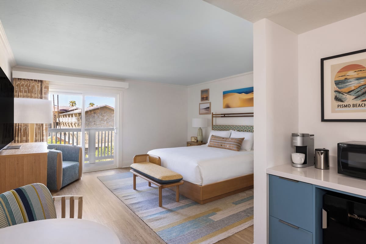 A hotel room with a bed, a desk, a TV, a coffee maker, and a framed picture of Pismo Beach.