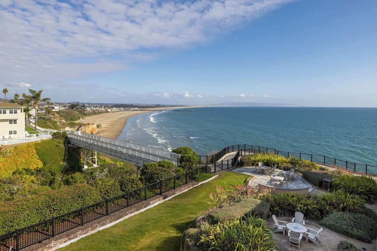 A coastal view with a beach, a bridge, and a patio area with outdoor seating.