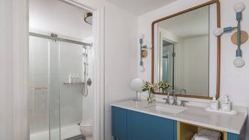 A modern bathroom with a glass-enclosed shower, a white sink with blue accents, and a large mirror with round lights.