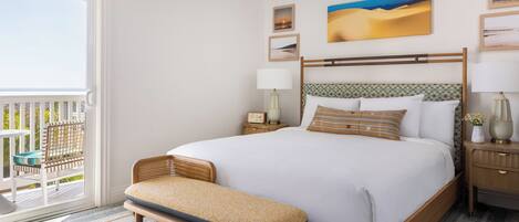 A hotel room with a large bed, a bench, a nightstand, a lamp, and a view of the outdoors.