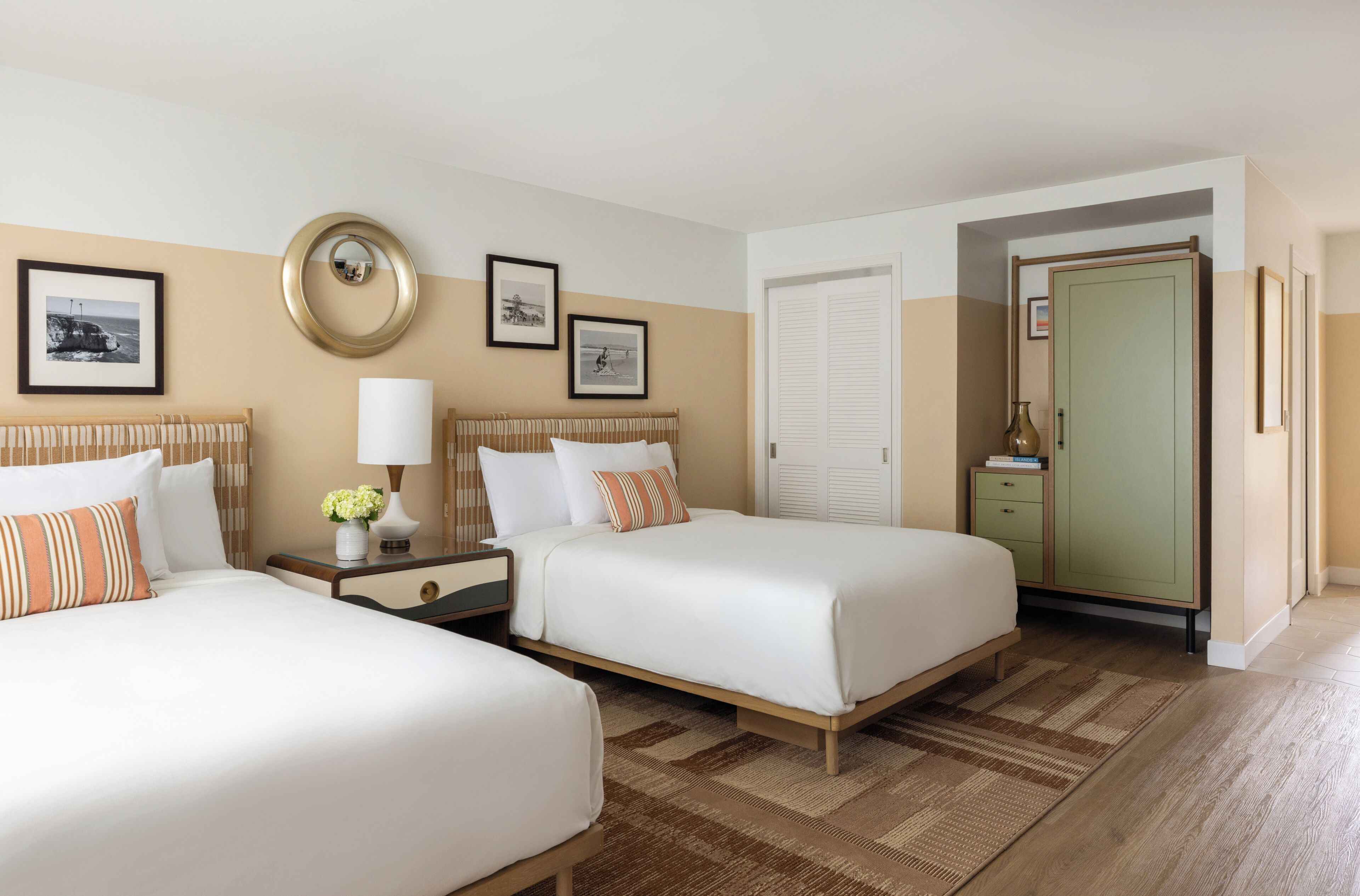 A hotel room with two beds, a nightstand with a lamp, a dresser, and a door leading to another room.