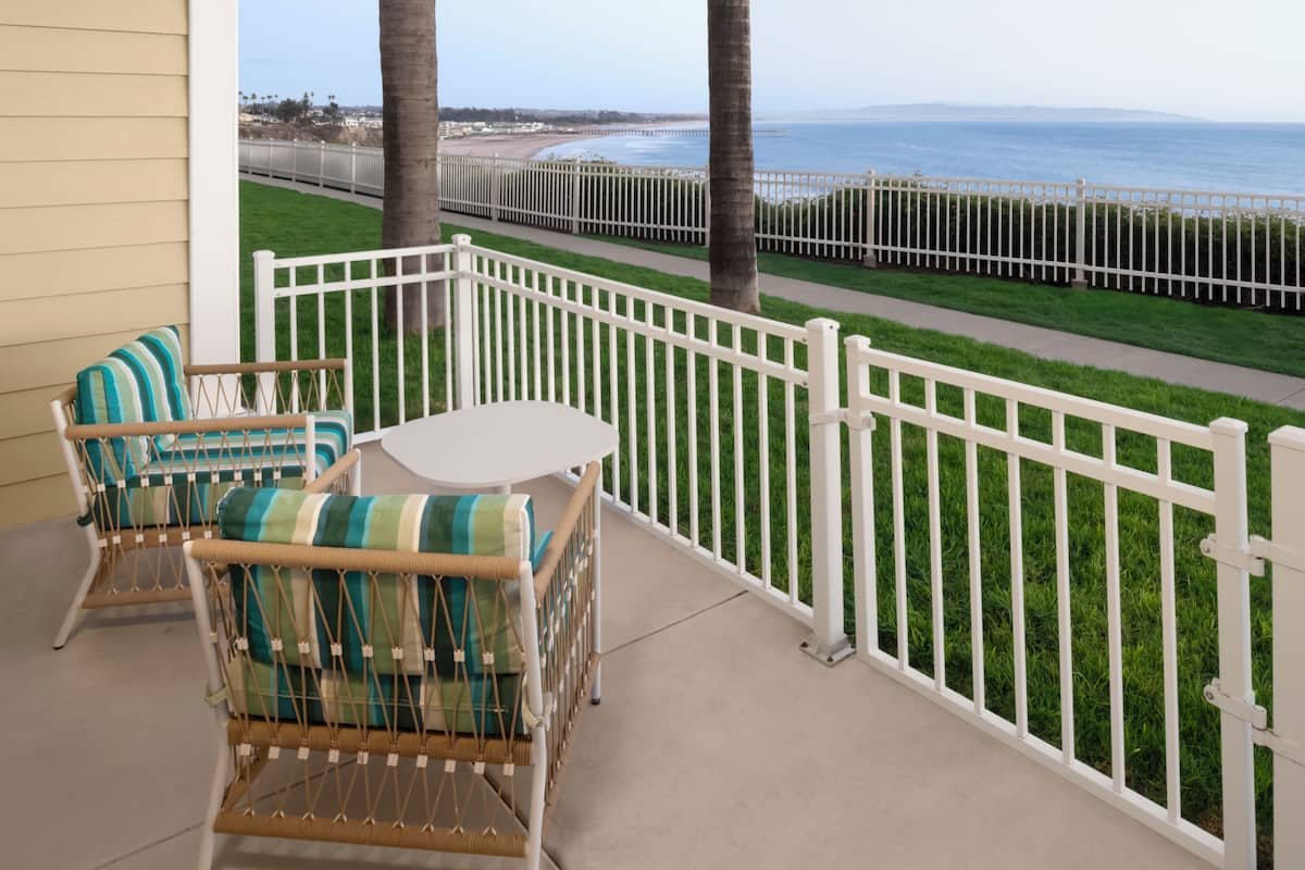 A balcony with wicker chairs, a small table, and a white fence overlooking a beach.