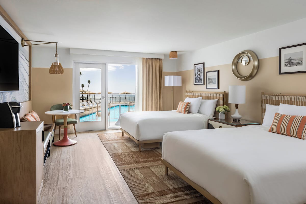 A hotel room with two beds, a desk, a chair, a TV, a pool view, and a balcony.