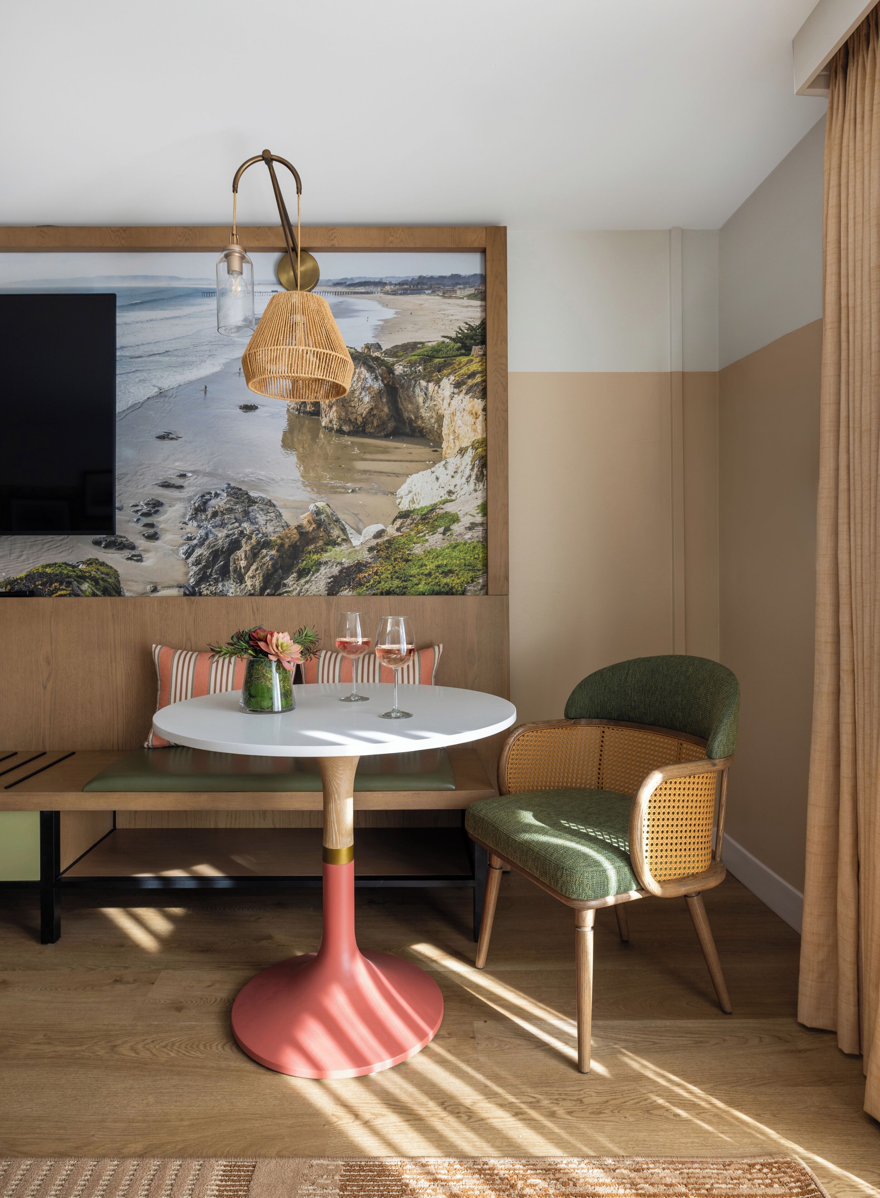 A dining area with a round table, chairs, a wall-mounted TV, and a large framed beach photograph.