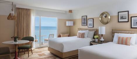 A hotel room with two beds, a dining area, and a balcony with a view of the sea.