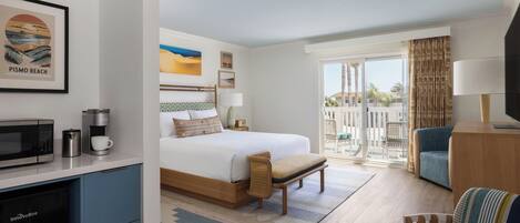 Habitación de hotel con cama, escritorio con microondas, cafetera, silla, televisor y balcón con vistas.