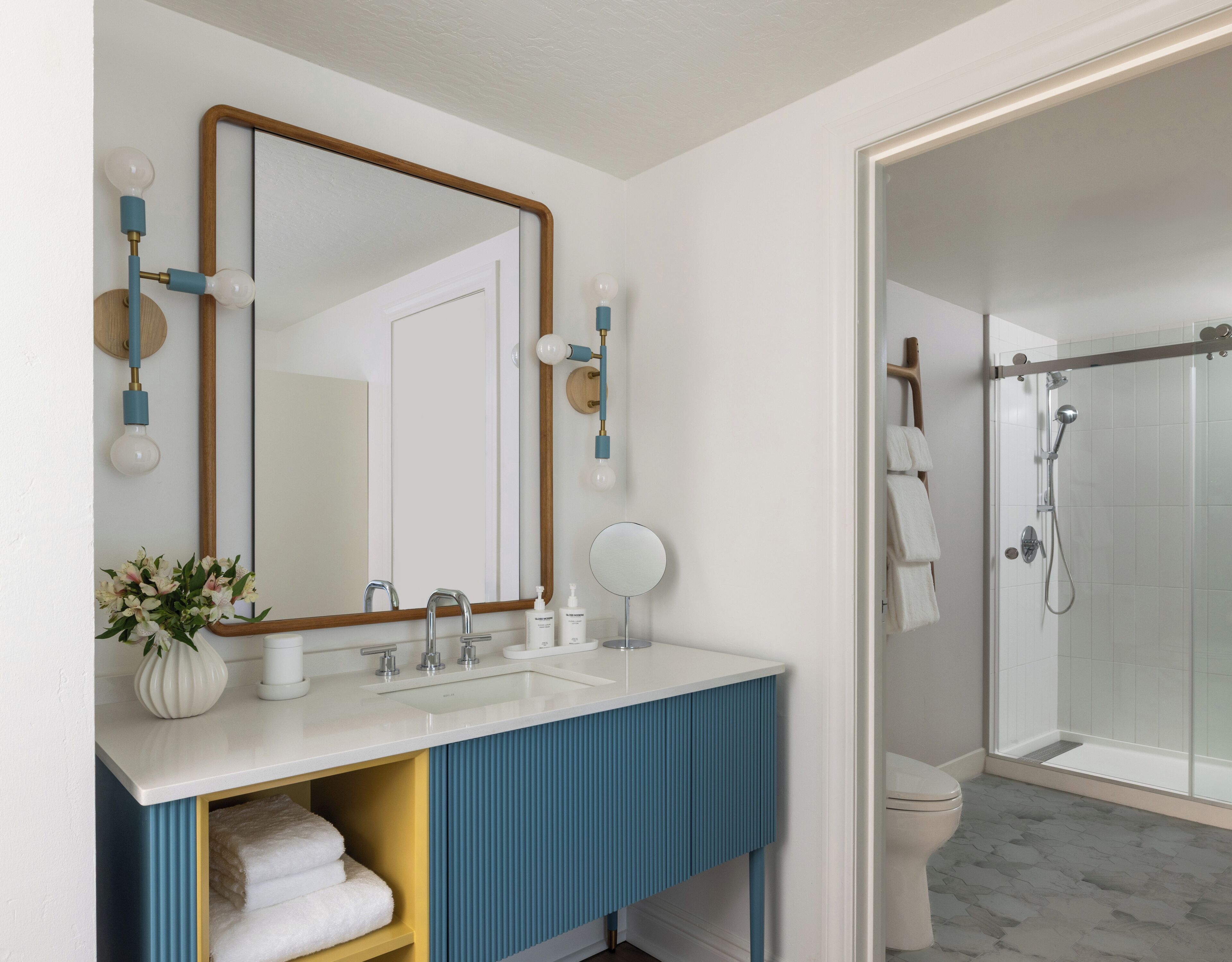 Une salle de bain avec un lavabo blanc, un meuble-lavabo bleu, un grand miroir, une douche et des toilettes.