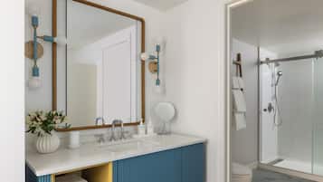 A bathroom with a white sink, blue vanity, a large mirror, a shower, and a toilet.