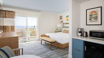 Habitación de hotel con cama, escritorio, banca, kitchenette y un gran ventanal con vista a la playa.