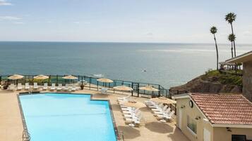 A pool with lounge chairs and umbrellas, overlooking a beach and ocean.
