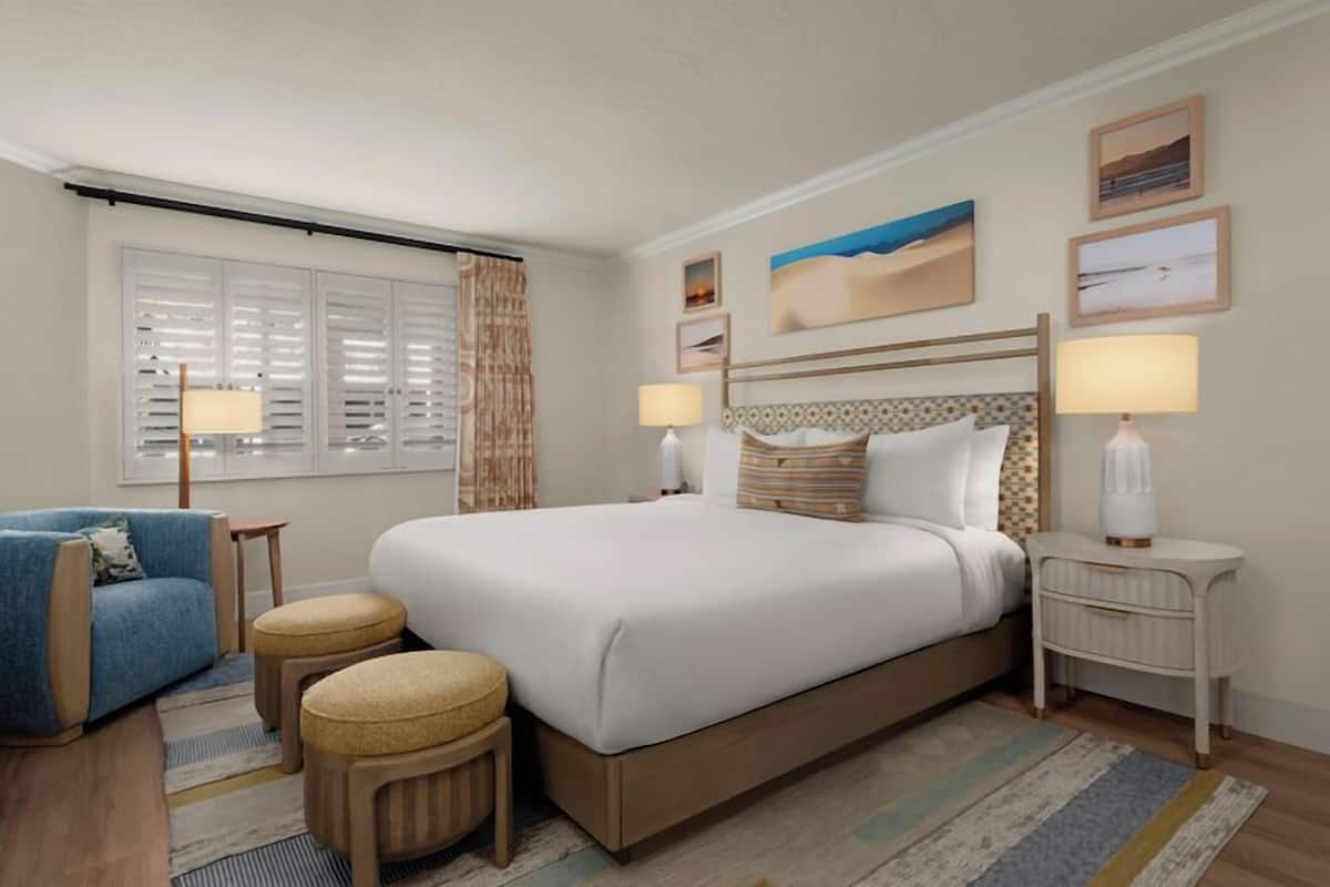 A hotel room with a large bed, two bedside tables, a chair, and a window with blinds.