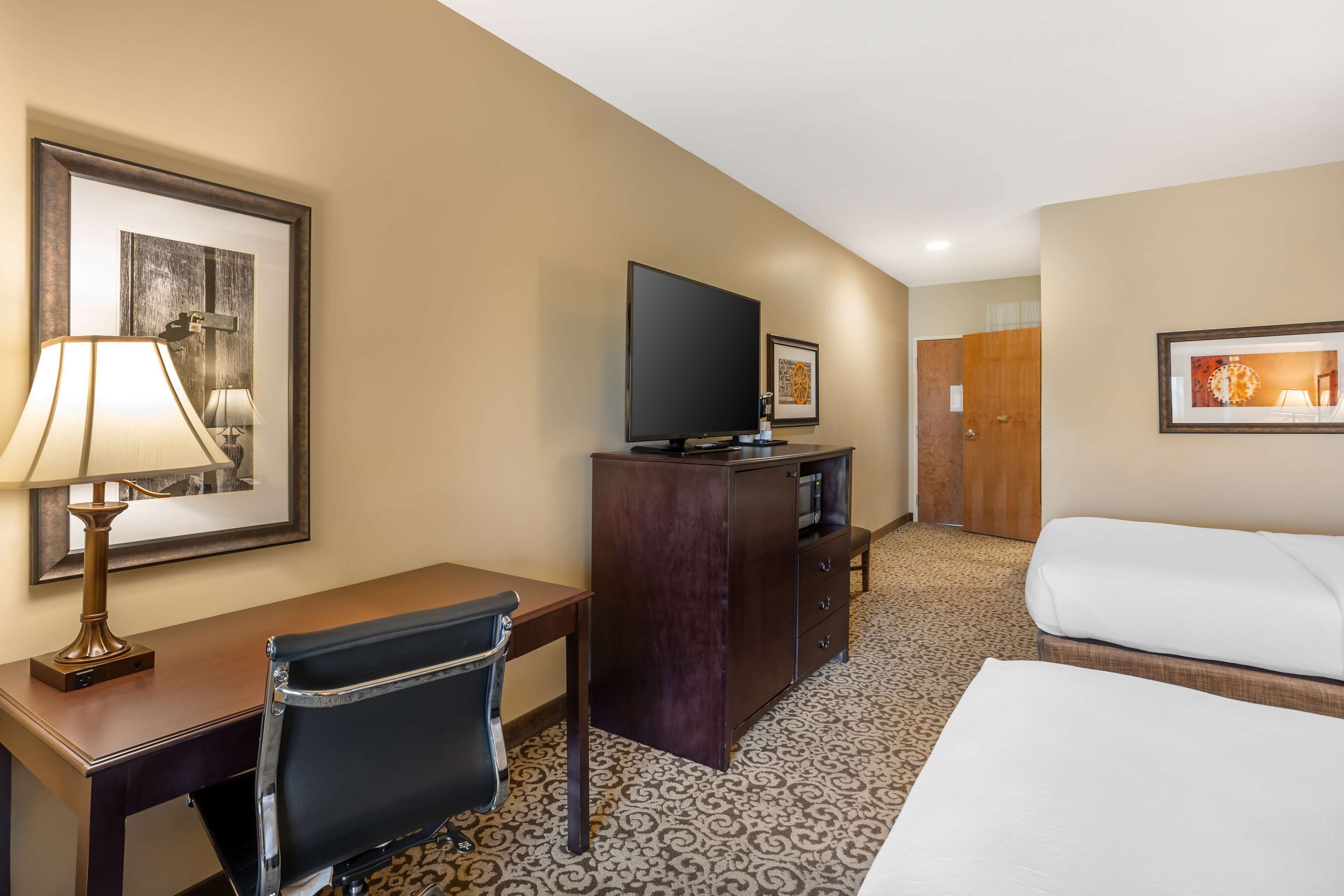 A hotel room with a bed, a desk with a lamp, a television, and a dresser.