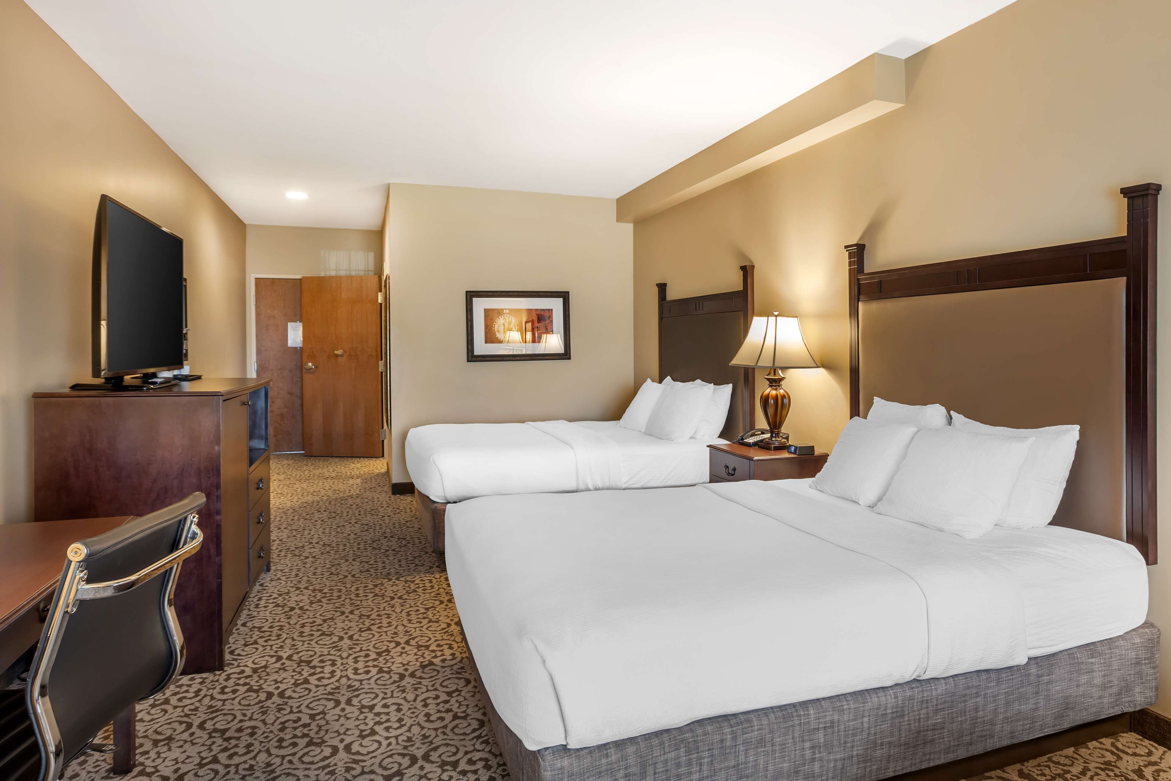 A hotel room with two beds, a desk, a television, and a framed picture on the wall.