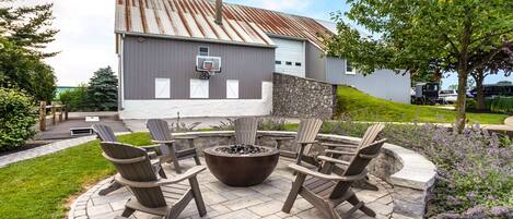 A patio with Adirondack chairs, a fire pit, and a stone wall.