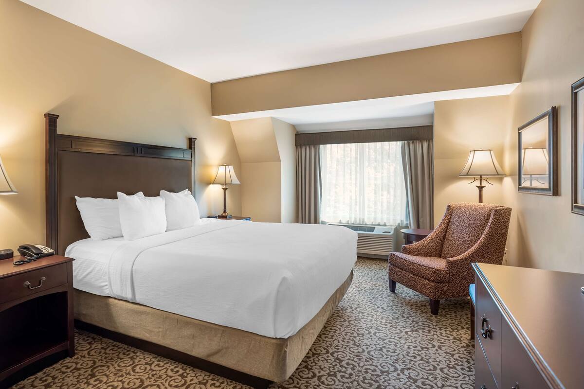 A hotel room with a large bed, a chair, a desk, and a window with curtains.