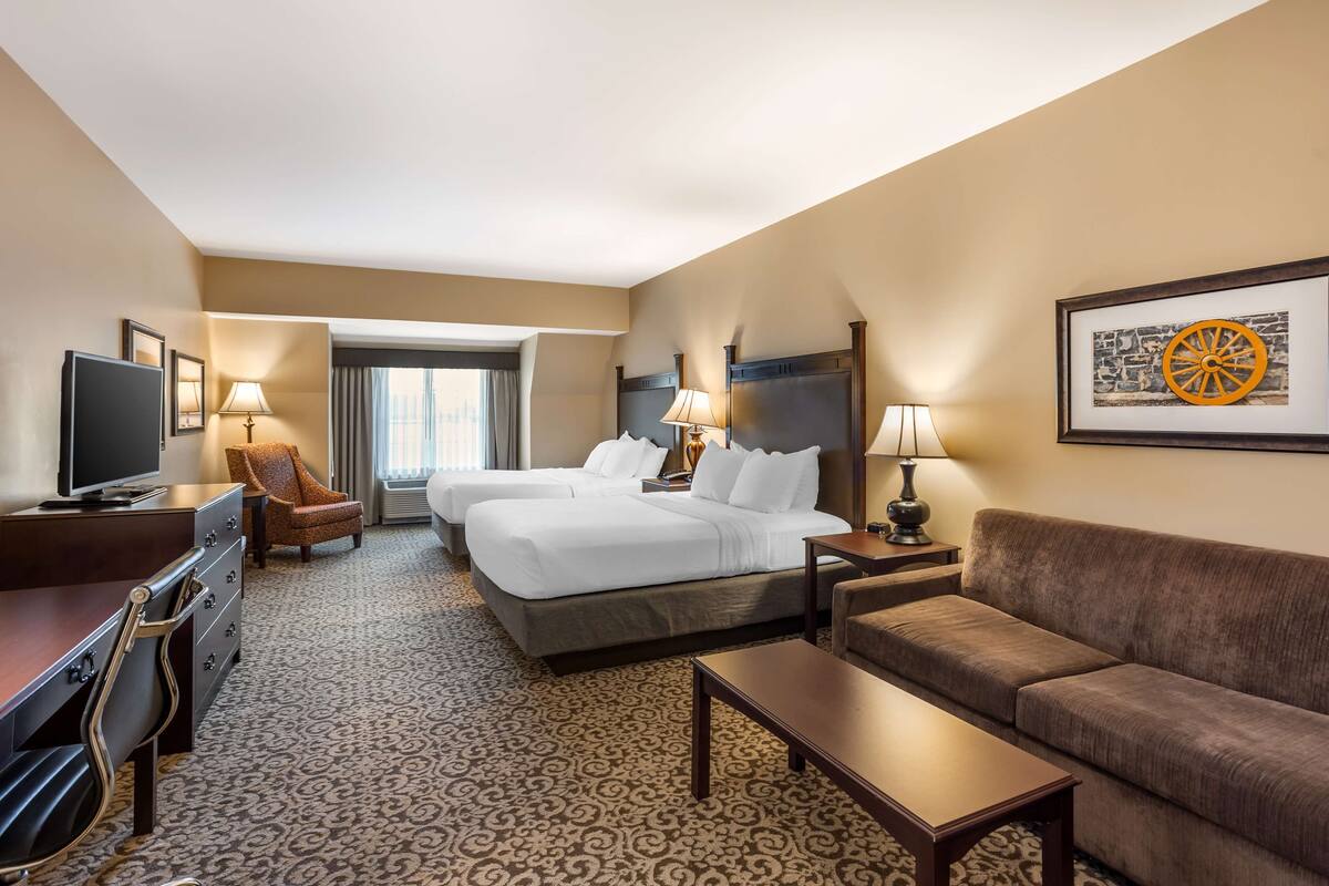 A hotel room with two beds, a sofa, a TV, a desk, and a lamp.