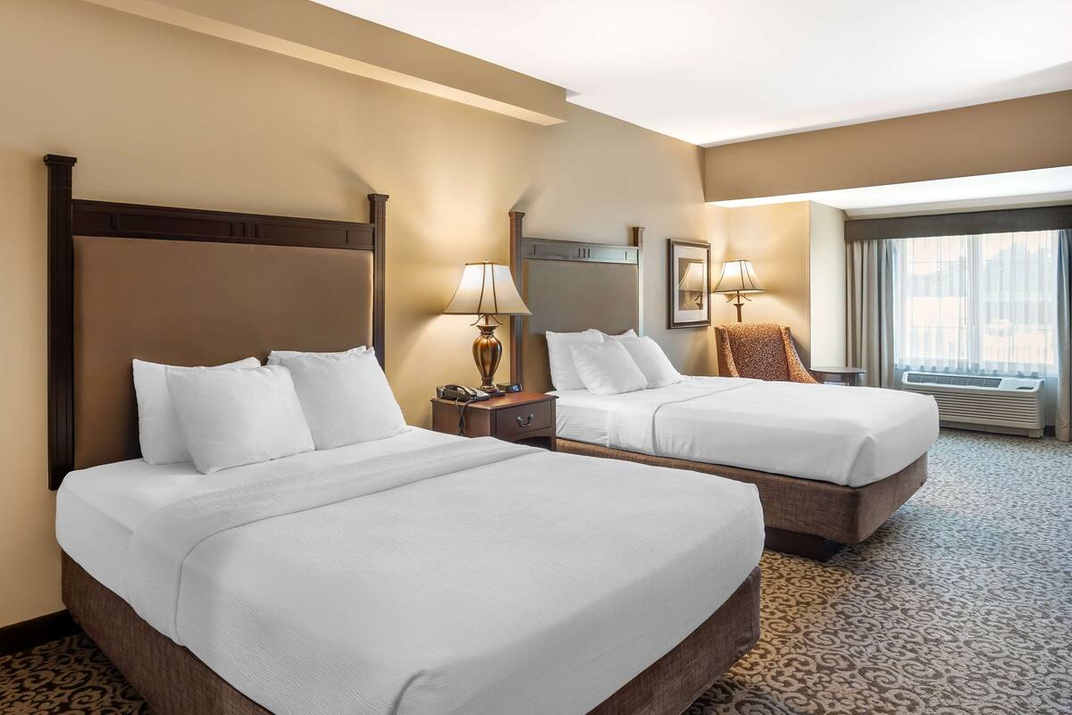 A hotel room with two beds, a large window, and a carpeted floor.