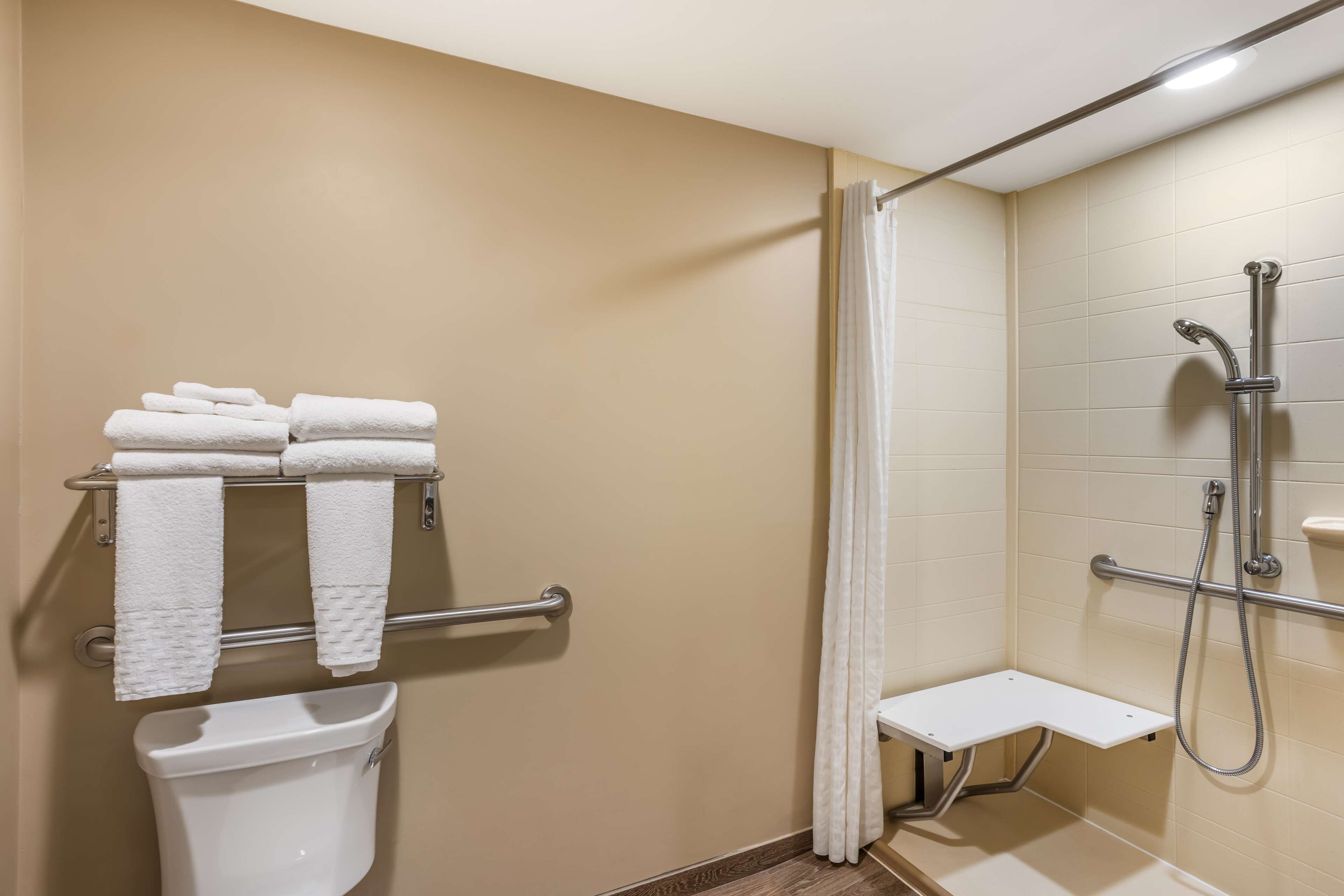 Un baño con inodoro, toallero con toallas, zona de ducha con ducha de mano y un pequeño banco.