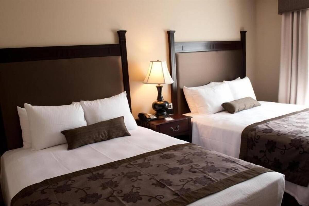 A hotel room with two beds, a nightstand with a lamp, and a window with curtains.