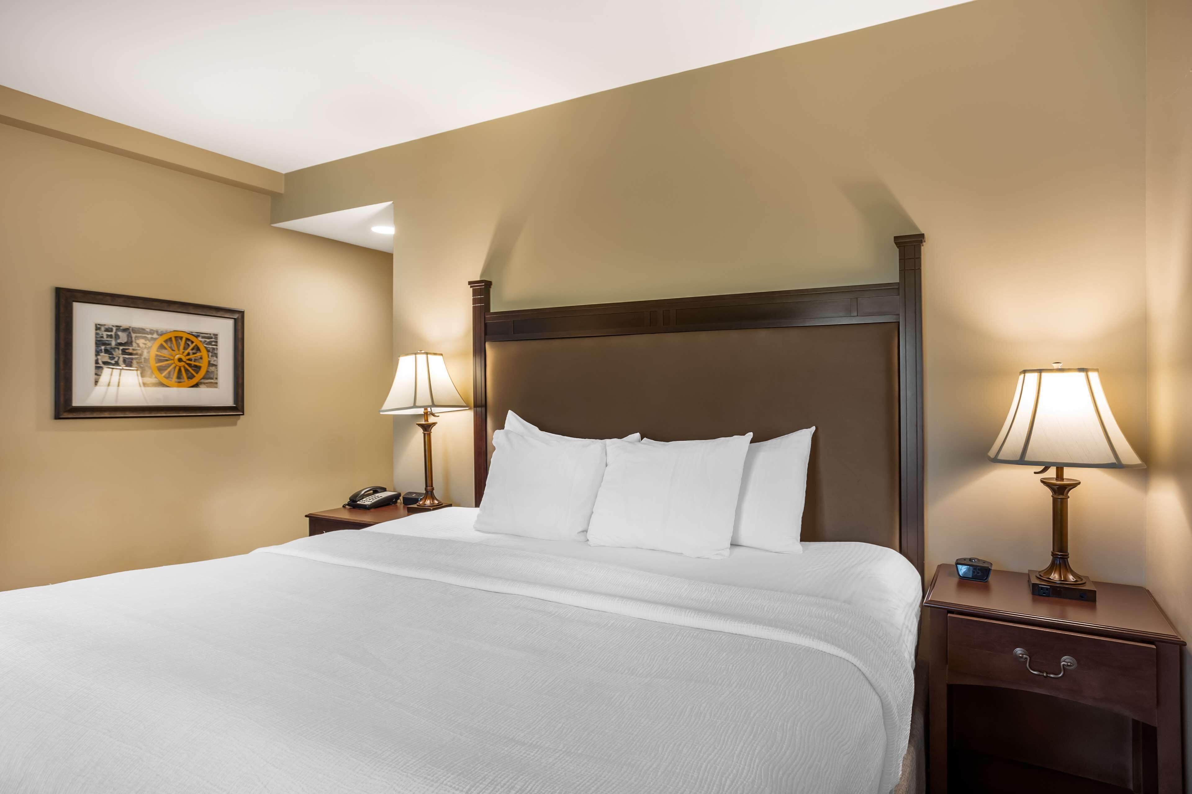 A neatly made bed with white linens, two bedside tables with lamps, a framed picture on the wall, and a wooden headboard.