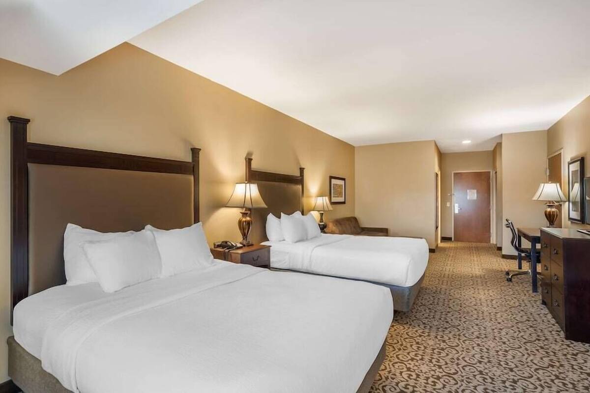 A hotel room with two beds, a desk, a chair, lamps, and a carpeted floor.