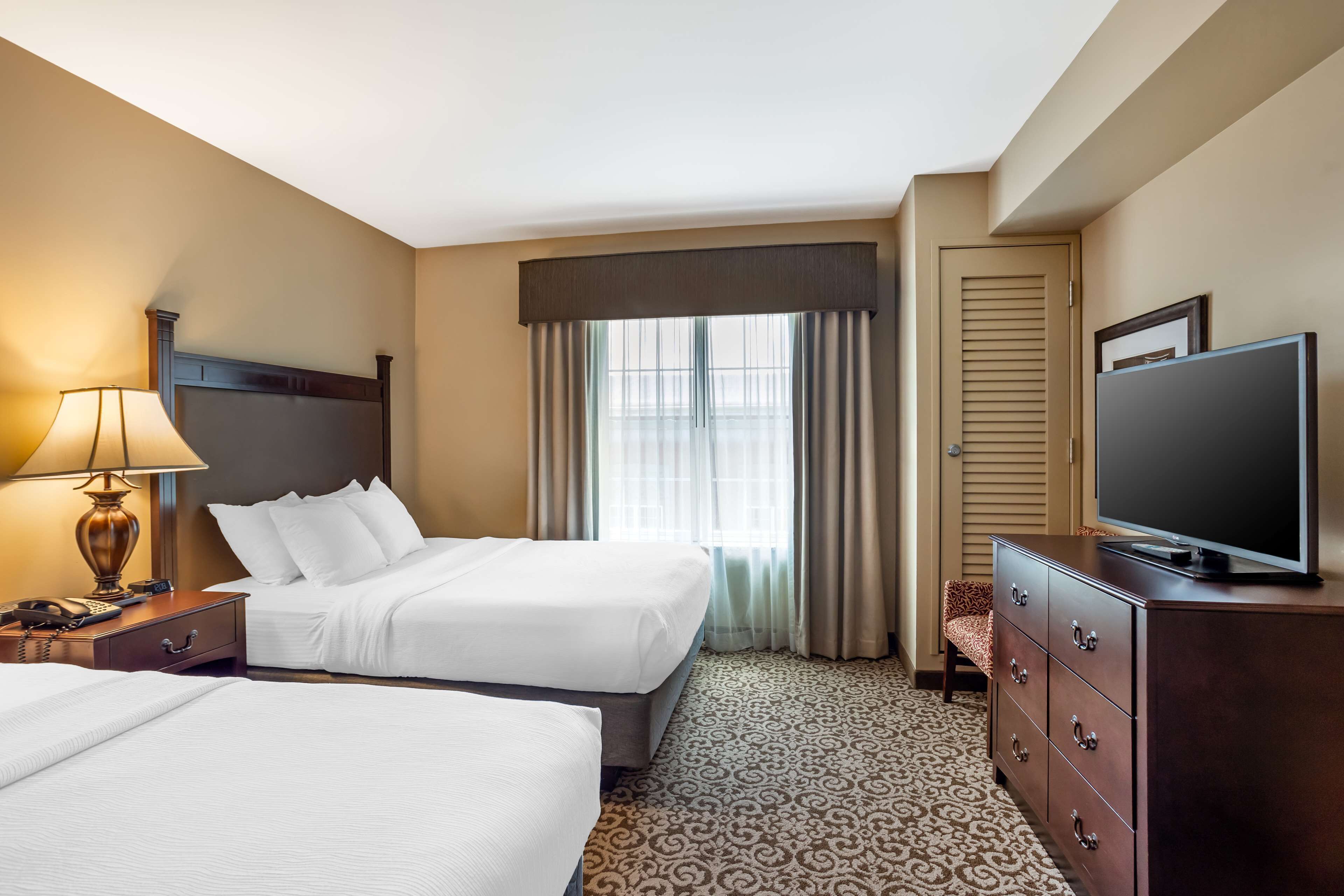 A hotel room with two beds, a television, a lamp, and a dresser.