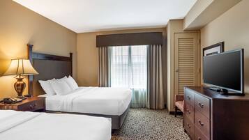 A hotel room with two beds, a television, a lamp, and a dresser.