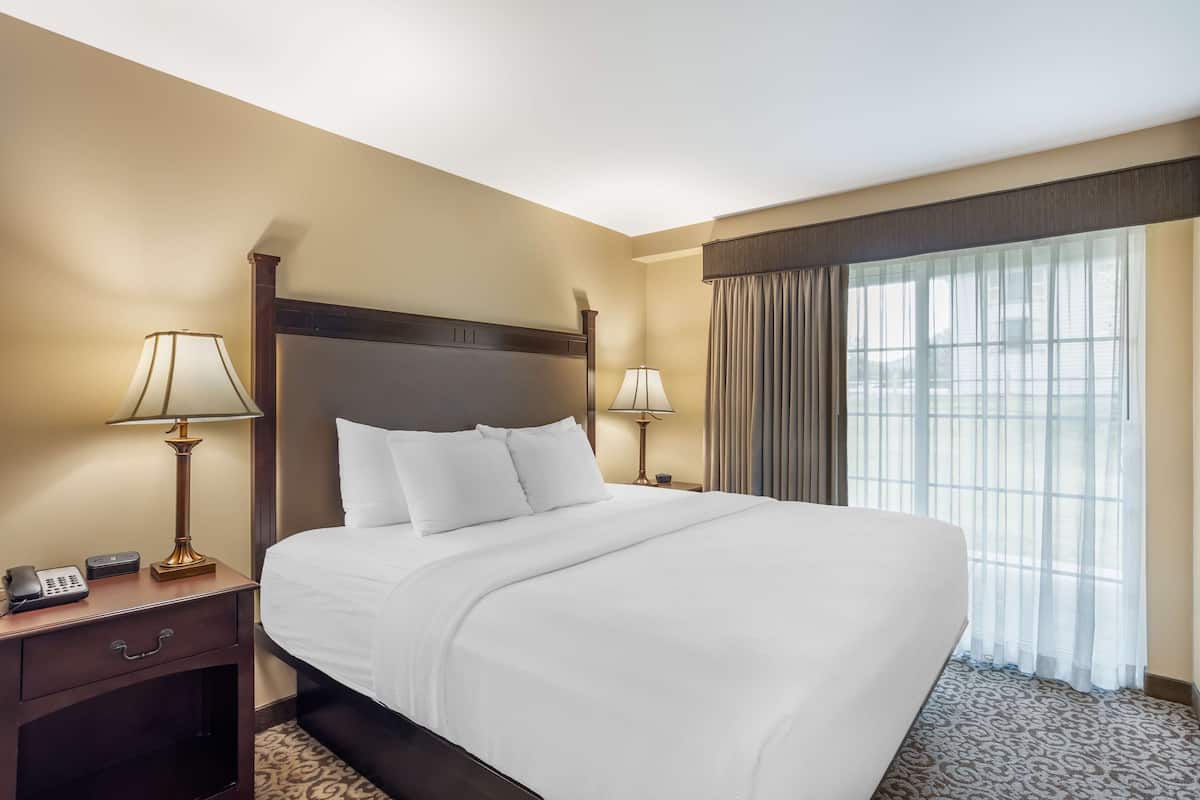 A hotel room with a large bed, two bedside tables with lamps, a telephone, and a window with curtains.