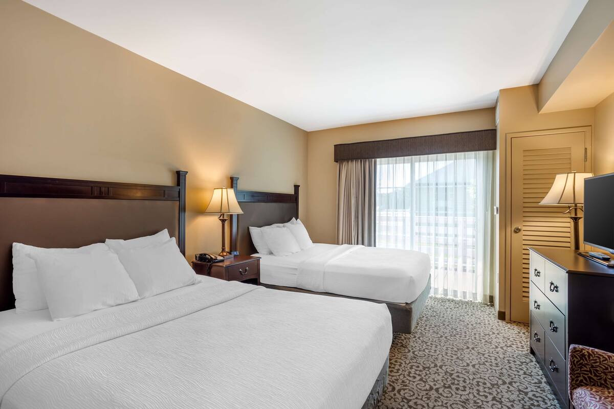 A hotel room with two beds, a dresser, a TV, and a window with curtains.