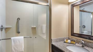 Une salle de bain dotée d’une douche à parois de verre, d’un porte-serviettes, d’un lavabo avec un plan de travail en granit et d’un miroir avec un cadre en bois.