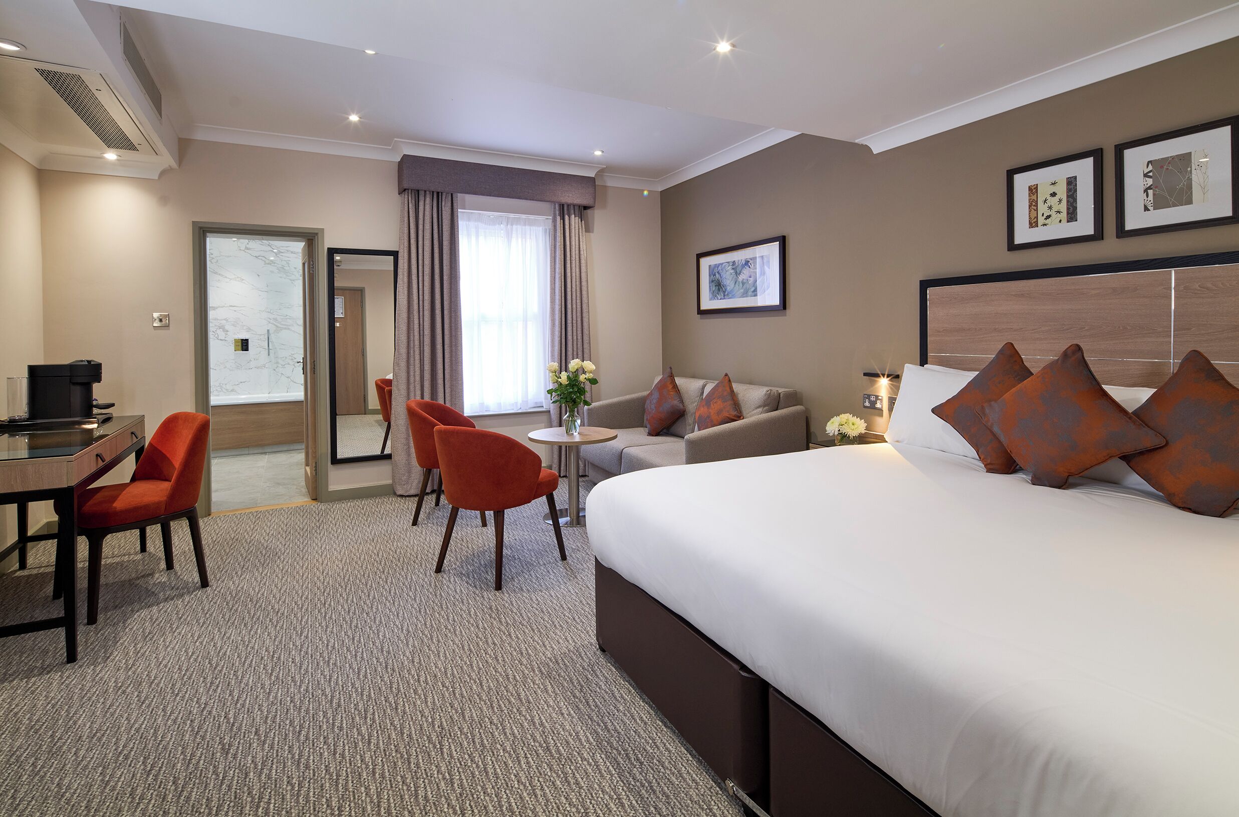 A hotel room with a large bed, a desk, two chairs, a sofa, and a small table.
