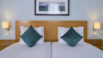 A hotel room with two beds, each with white bedding and teal pillows, a wooden headboard, and a framed picture on the wall.