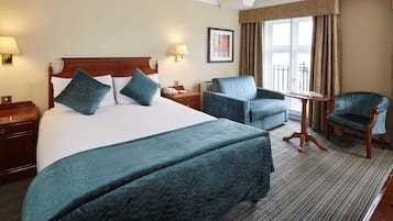 A hotel room with a large bed, two armchairs, a small table, and a view of the outdoors through a window.