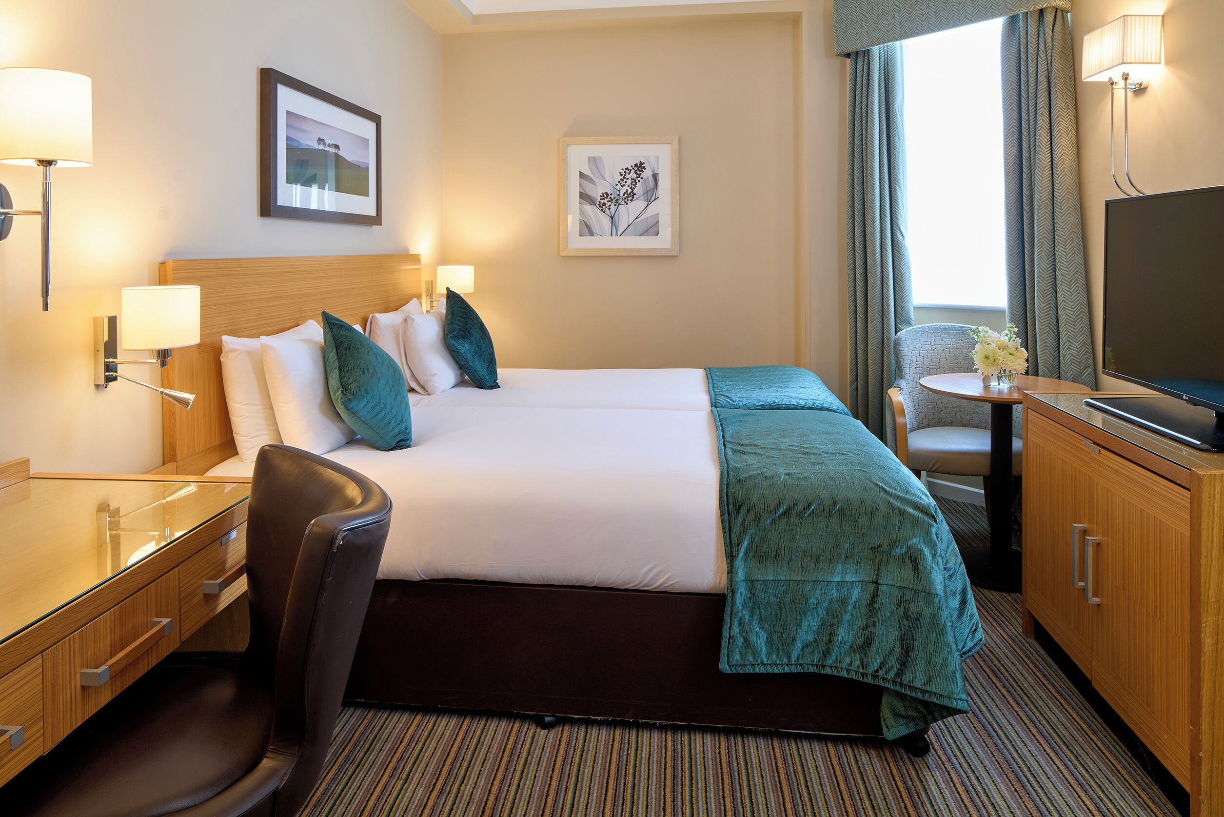 Une chambre d’hôtel équipée d’un lit, d’un bureau, d’une chaise, d’une télévision et d’une fenêtre avec des rideaux.