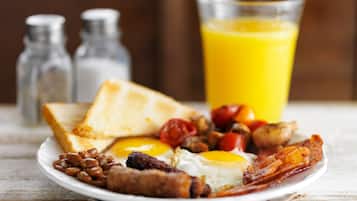Un plato de desayuno con tostadas, huevos, tocino, frijoles y tomates, acompañado de un vaso de jugo de naranja.