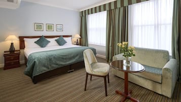 A hotel room with a bed, two bedside tables, a chair, a sofa, and a small table with a vase of flowers.