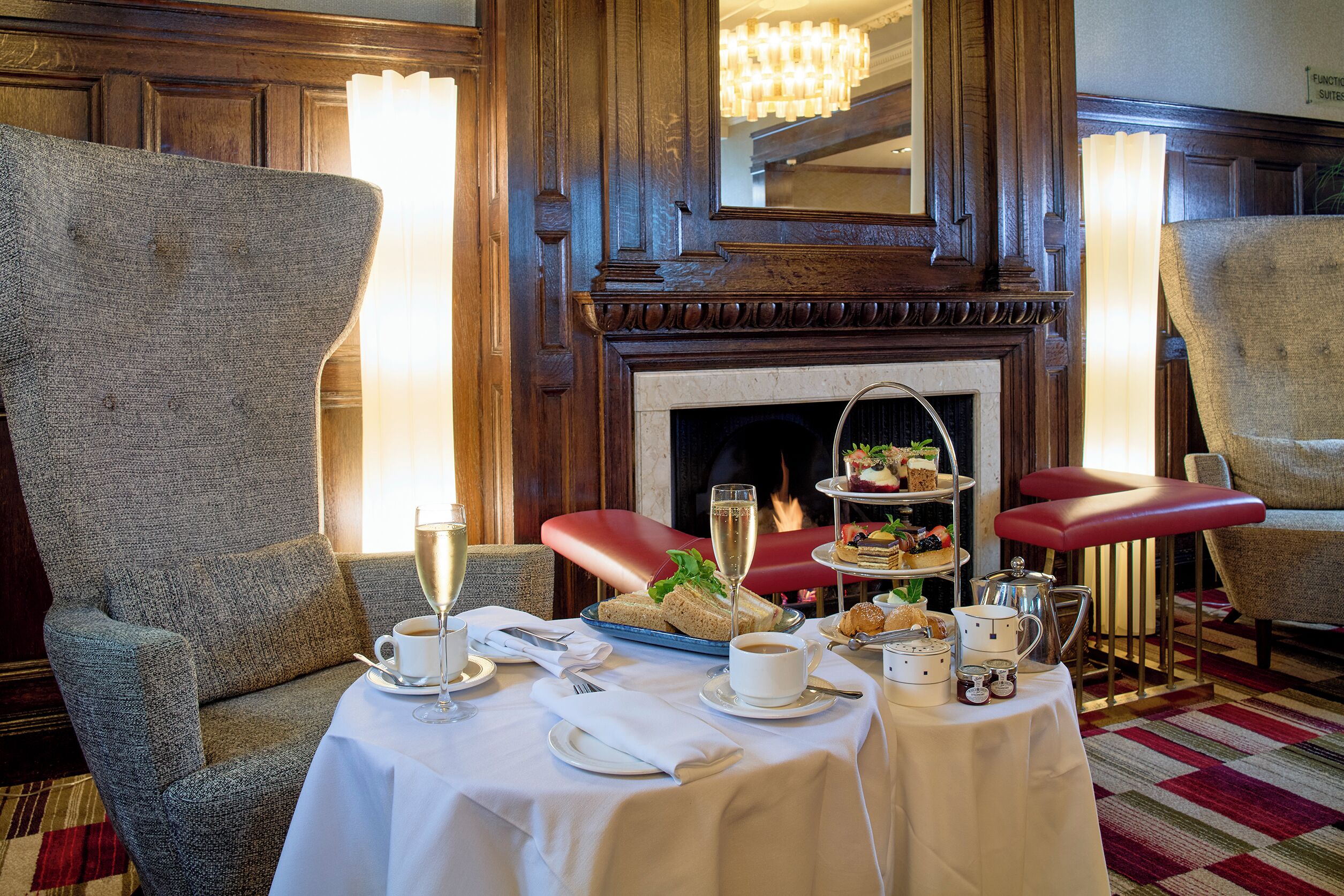 A dining area with a fireplace, a table set for two with a bottle of champagne, and a tray of sandwiches.