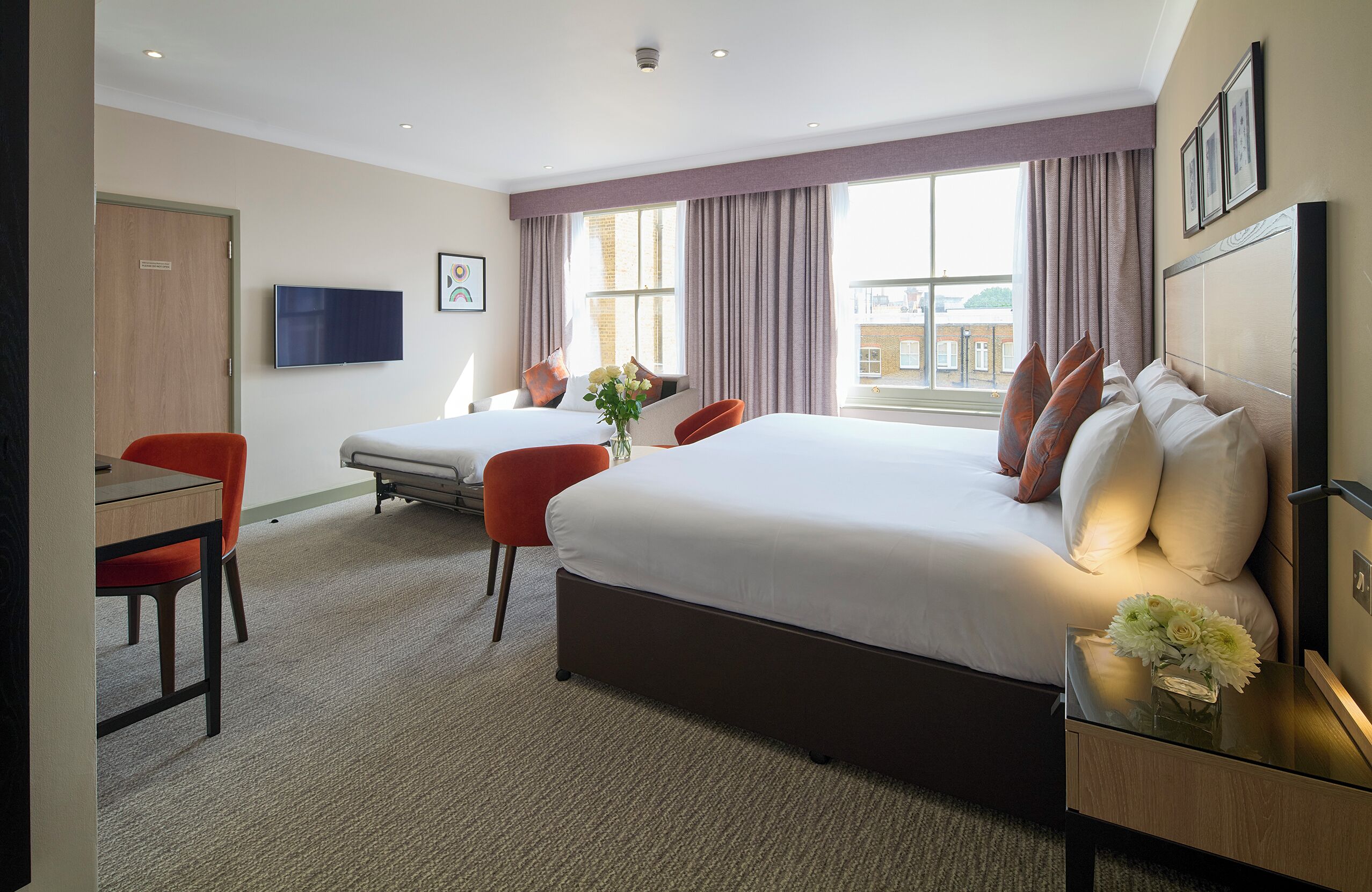 Quarto de hotel com duas camas, uma escrivaninha, uma cadeira, uma televisão e uma janela com cortinas.