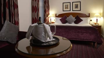 Ein Hotelzimmer mit einem ordentlich bezogenen Bett, zwei Nachttischlampen, einem runden Tisch mit Flasche und Gläsern sowie einem roten Teppich.