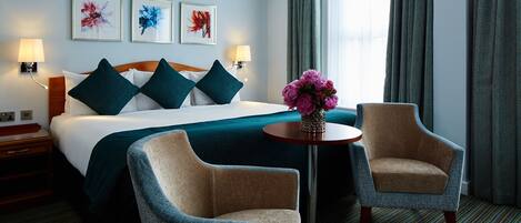 A hotel room with a large bed, two armchairs, a small table, and artwork on the wall.